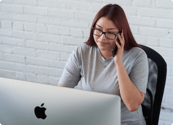 Woman sitting at a computer, holding a phone to her ear